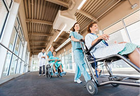Low angle view of female nurses pushing patients on wheelchairs with doctor walking at corridor in hospital