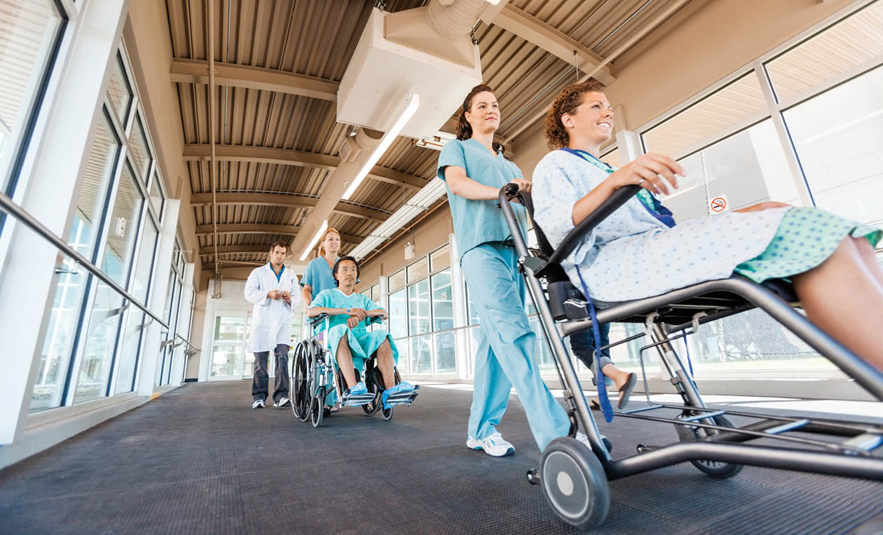 Low angle view of female nurses pushing patients on wheelchairs with doctor walking at corridor in hospital