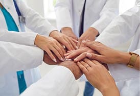 Team of doctors in white uniform standing in hospital or clinic putting their arms in a pile. Stack of medical staff hands. The concept of unity, partnership, teamwork and health care .