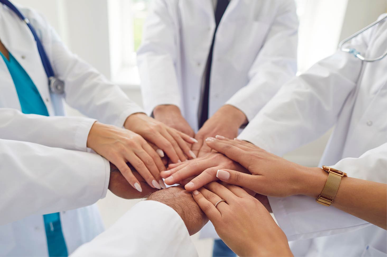 Team of doctors in white uniform standing in hospital or clinic putting their arms in a pile. Stack of medical staff hands. The concept of unity, partnership, teamwork and health care .